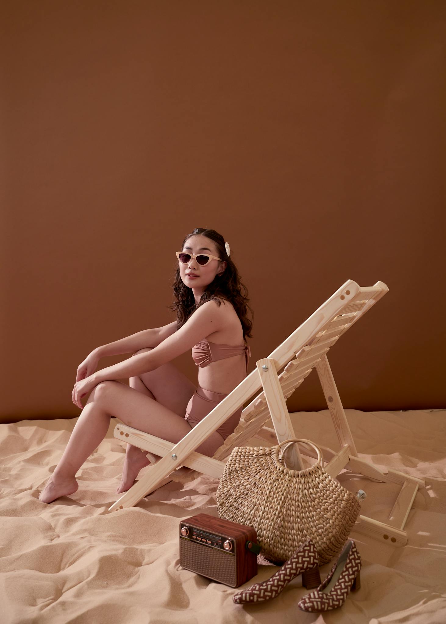 Elegant woman in swimsuit and sunglasses sitting on a beach chair with a retro vibe.